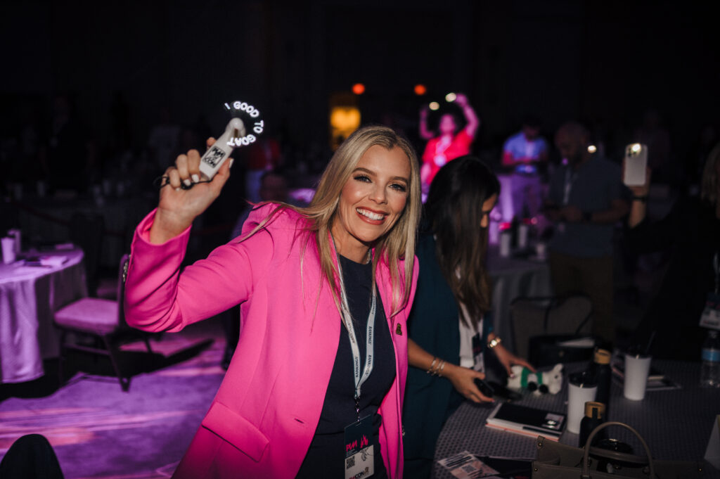 Female Personal Injury Lawyer holding up a fan displaying "from good to GOAT" at PIMCon